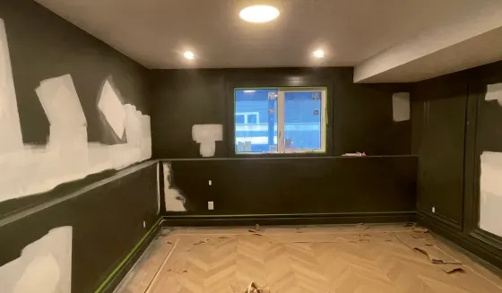 Filled and spot-primed drywall patches showing white against dark green walls in a Calgary room