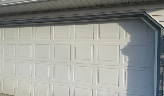 Panelled steel double garage door repainted warm grey with darker grey trim on an Airdrie home