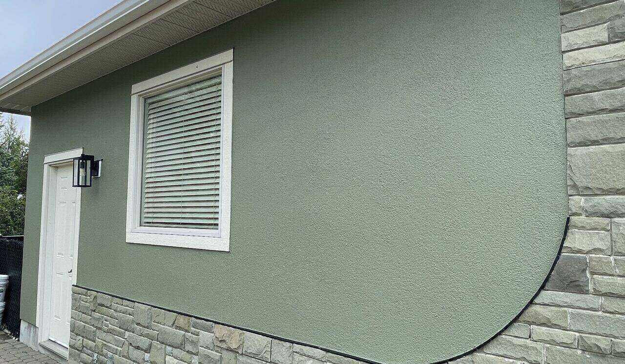 Finished sage stucco elevation with stone skirt and white trim on a Calgary home