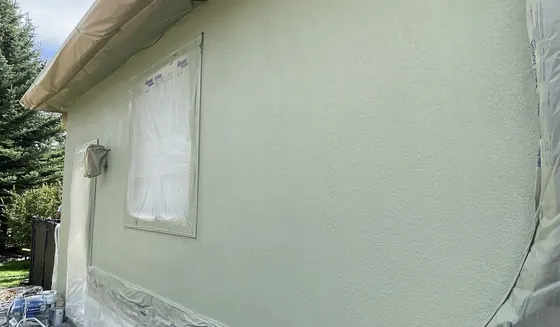 Stucco elevation masked and being spray-coated on a Calgary home