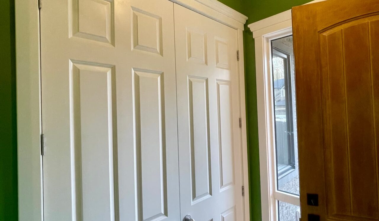 White panelled closet doors and casing beside a green wall in a Calgary entry