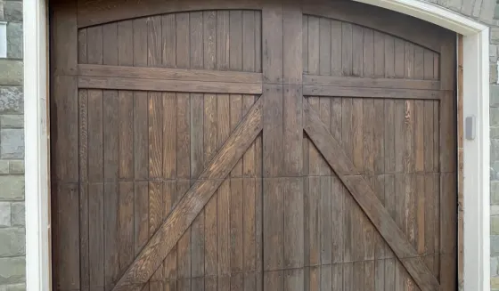 Arched wooden carriage-style garage door in a stone-clad Calgary home, refinished in a dark stain